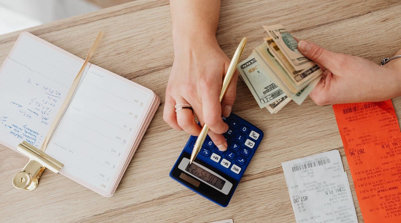 Hands counting banknotes next to a calculator, receipts and an open notebook